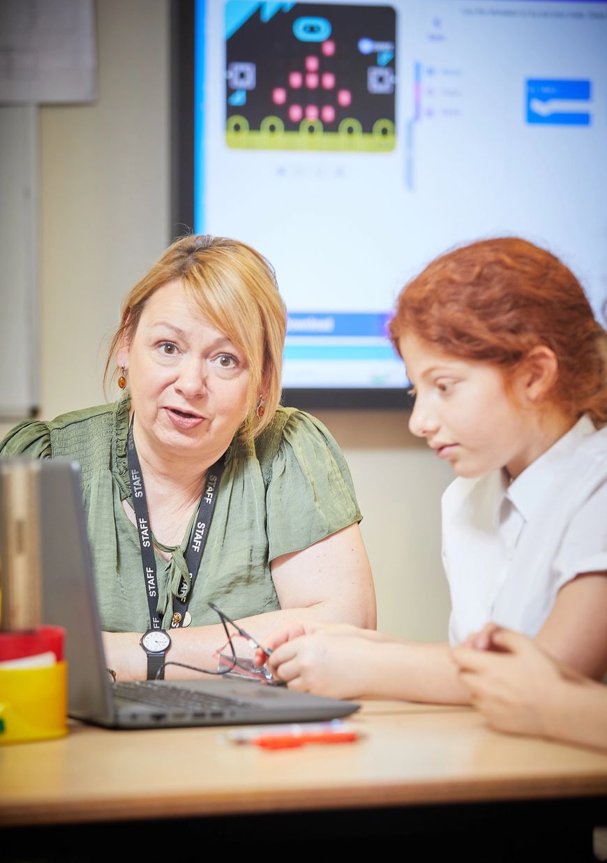 Mestra asseguda amb un alumne explicant com funciona la micro:bit